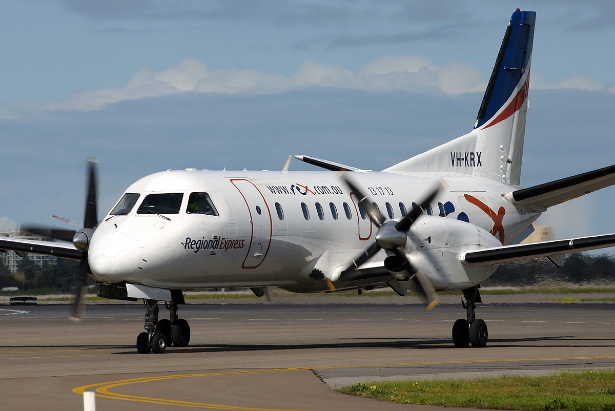 A small plane with spinning propellers taxis on a runway.